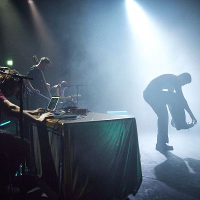 A dancer on stage performing with a spotlight on them with a student sat behind a sound desk on a laptop to the left of the dancer